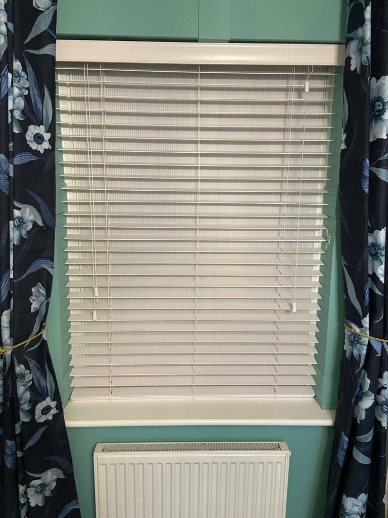 White Venetian blinds installed in Northamptonshire bedroom with floral curtains providing adjustable light control and layered window privacy solution