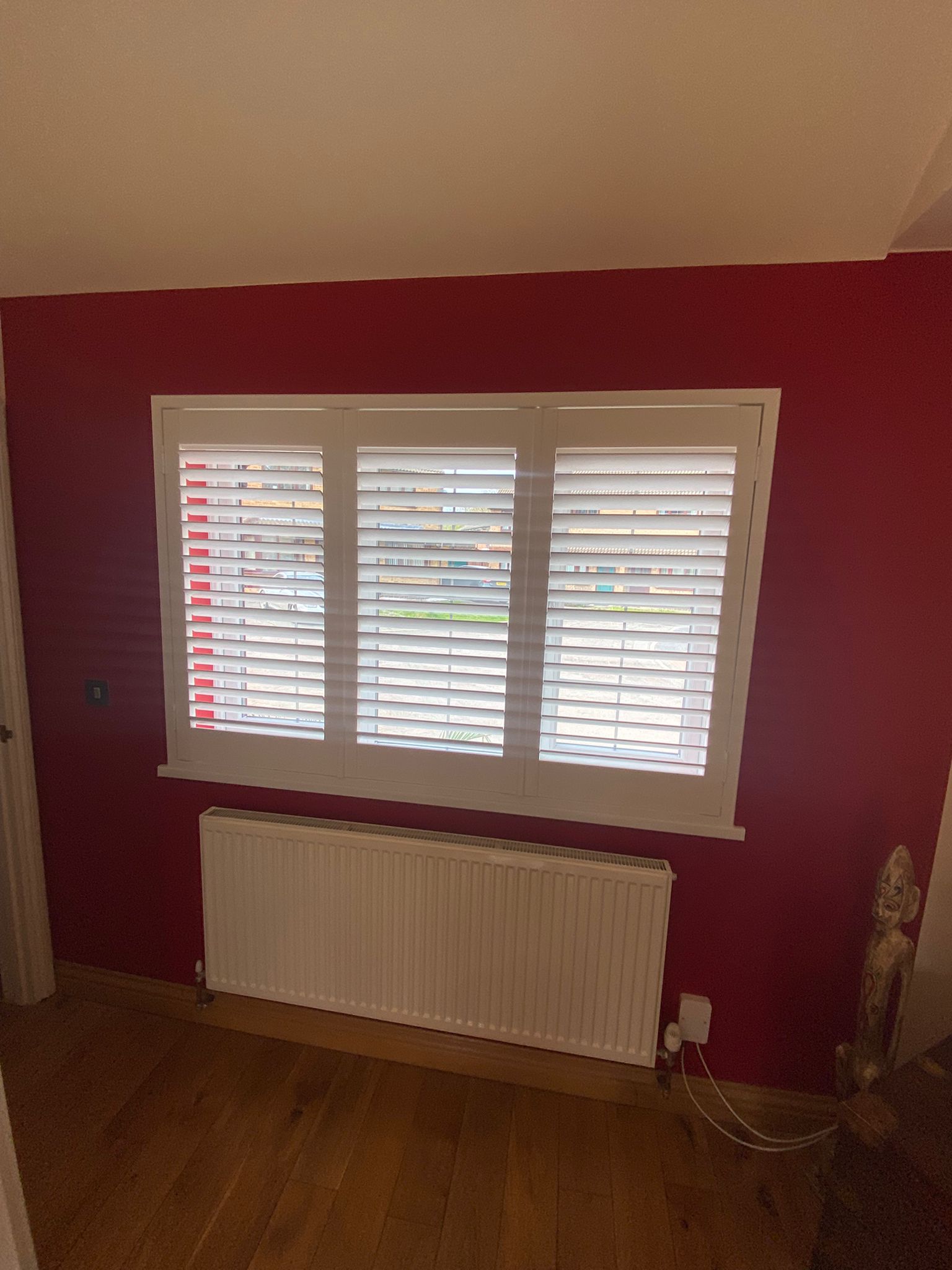 White plantation shutters installed in Daventry dining room providing adjustable privacy and natural light control against bold red feature walls