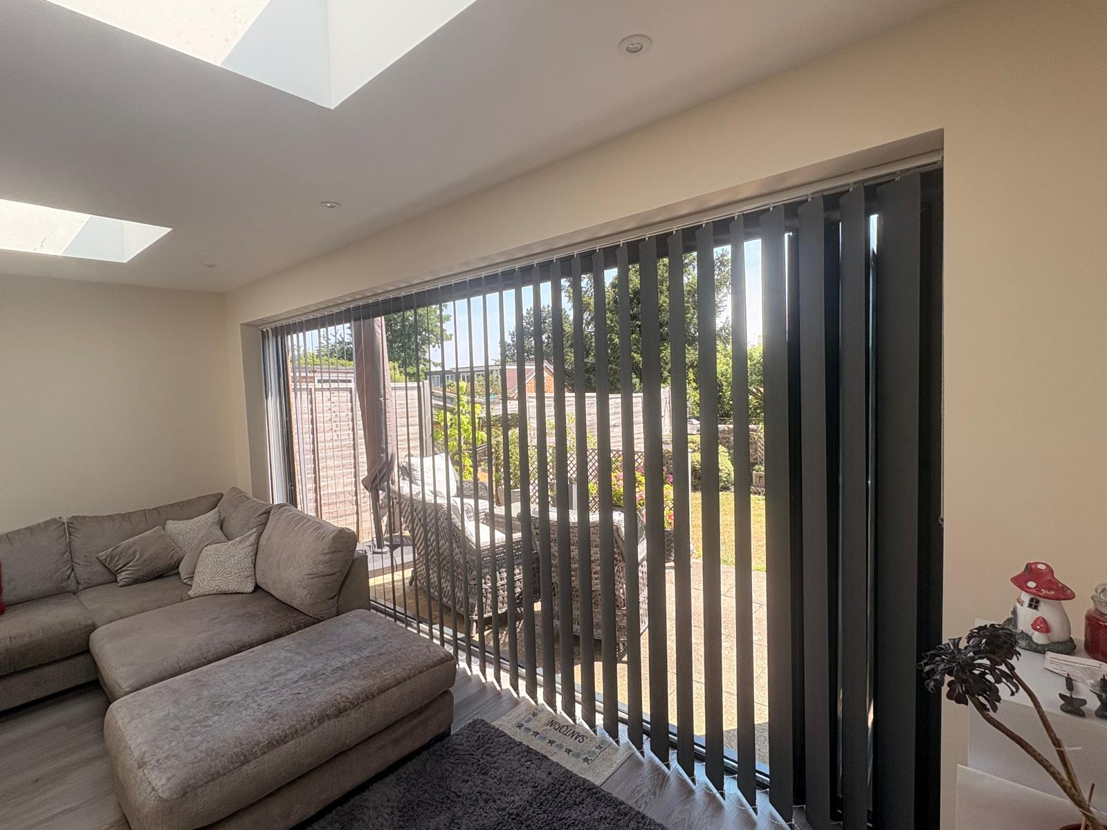 Blackout vertical blinds tilted for light control on a wide window in Wootton