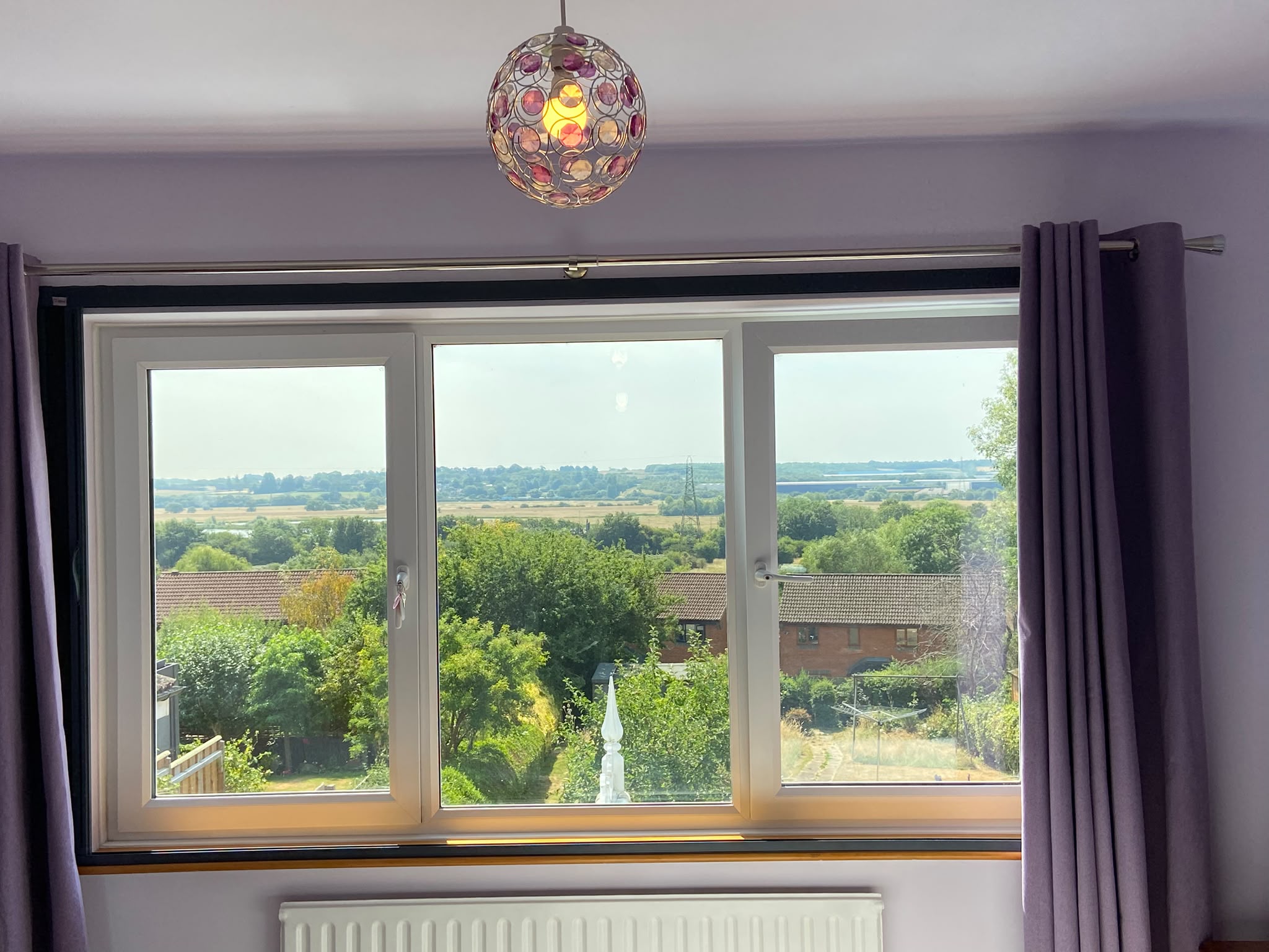 Retracted Blind Screen fitted outside the recess of a three-panel window with purple curtains in Northampton